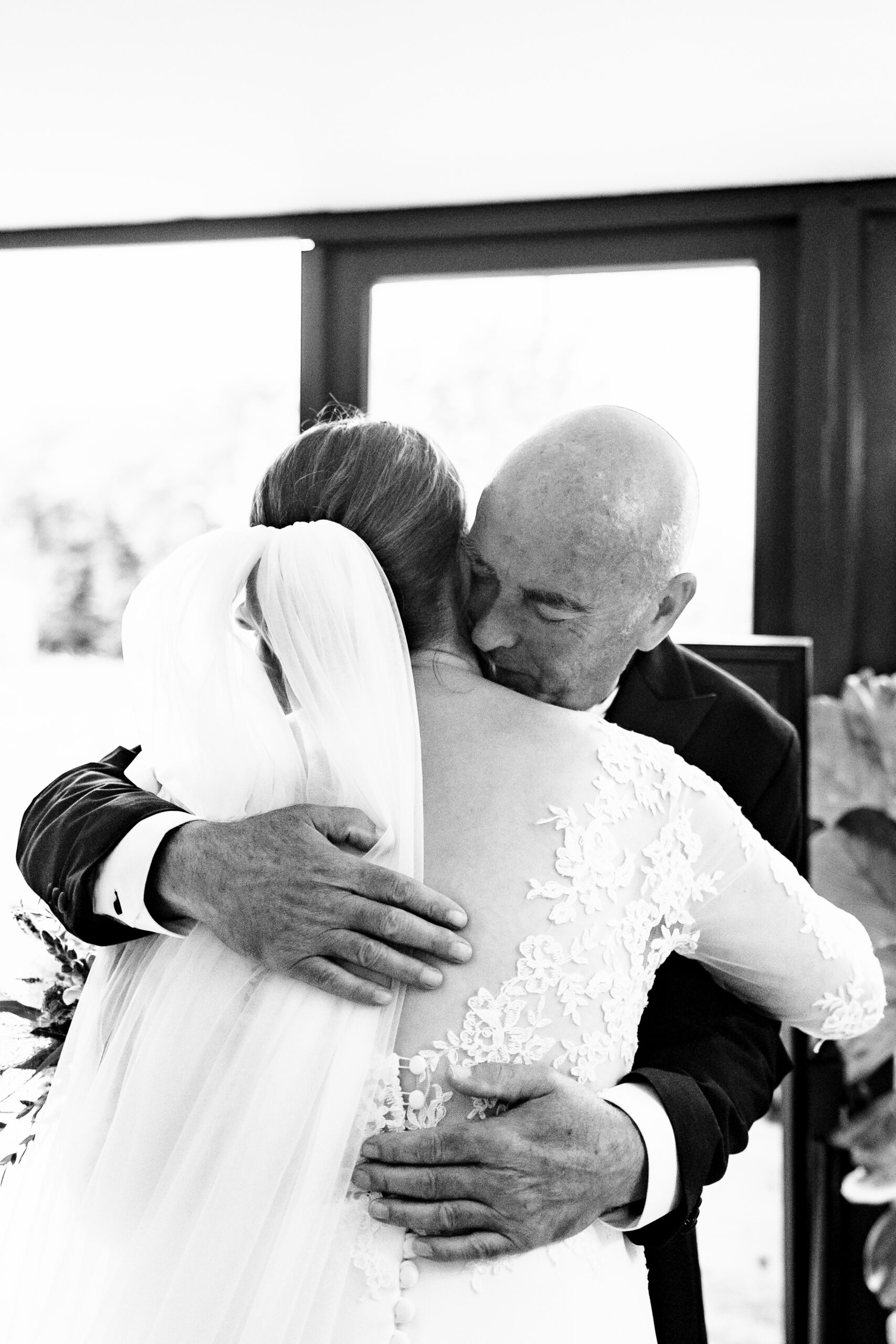 A black and white image of the bride and her father hugging. He is closing his eyes and they are embracing tightly.