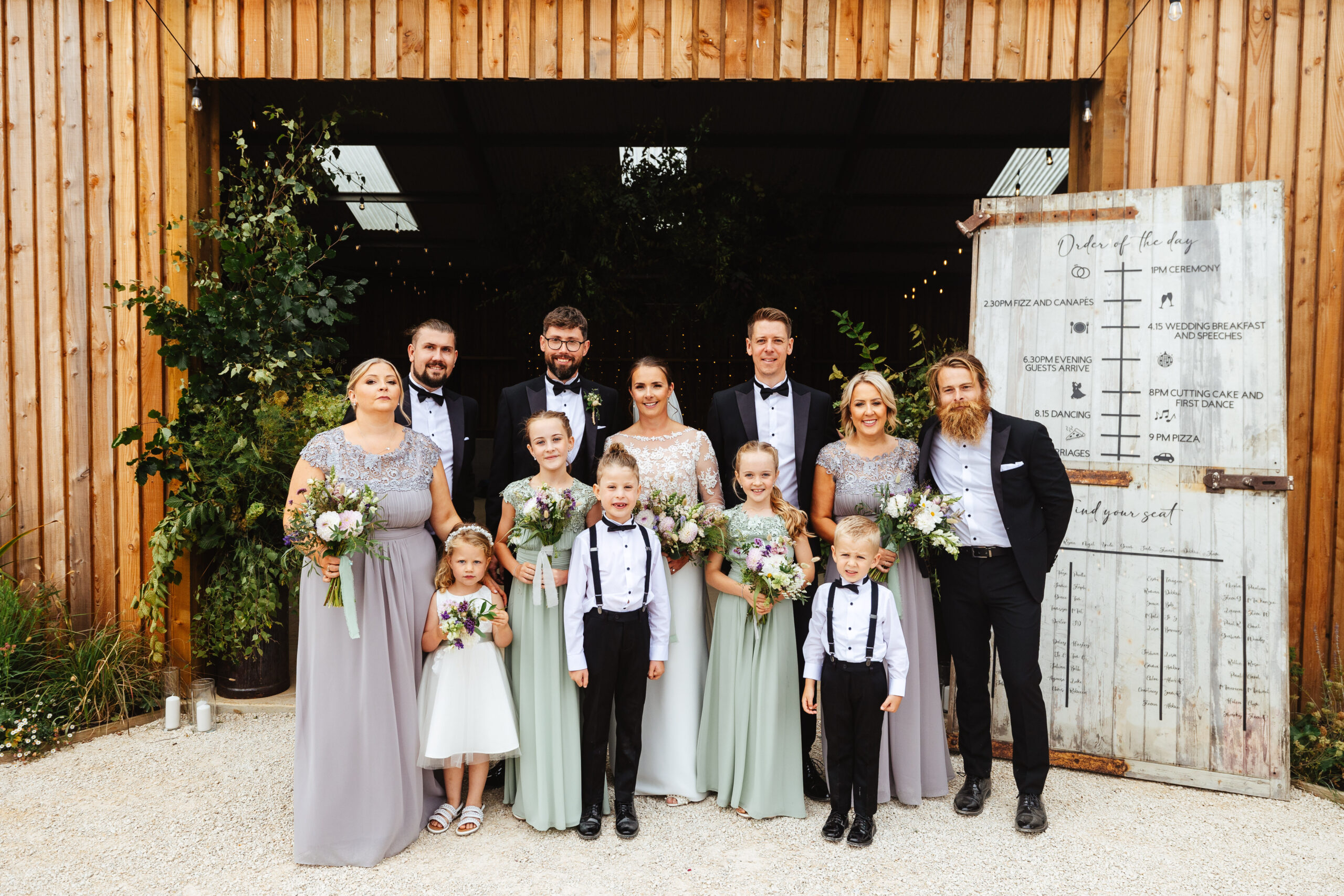 The bridal party in front of the barn. They are all looking at the camera and smiling.