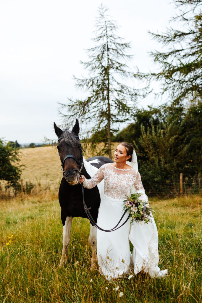 bride walking through long grass in a white bridal dress, with her brown horse by her side