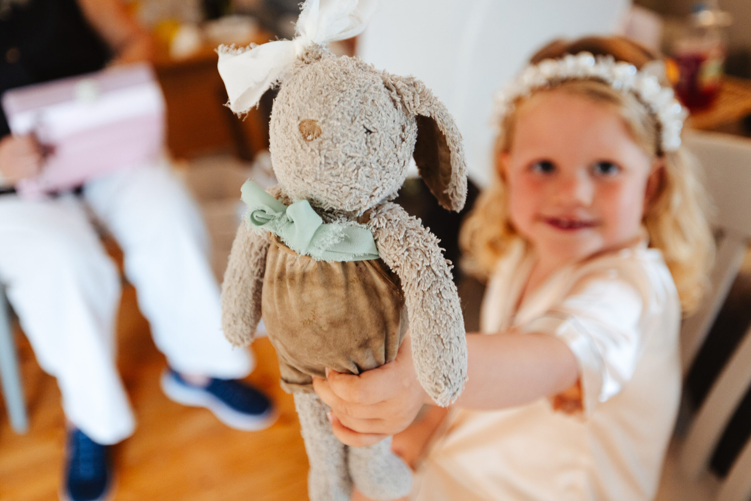 A little girl in white silk pyjamas. She is holding a tatty rabbit teddy bear and is smiling. She is out of focus, but you can see she is happy.