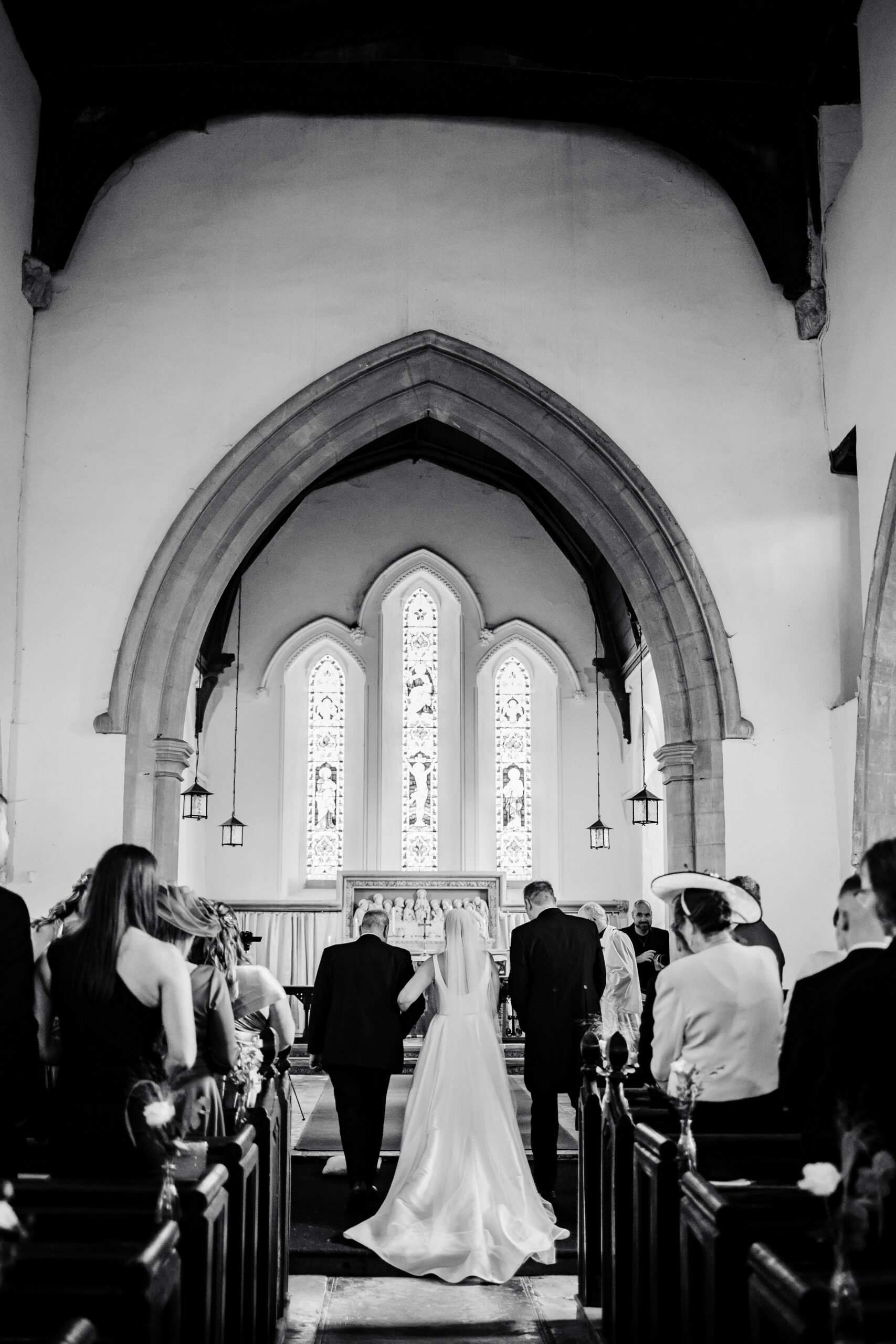 A black and white image of the bride and her father walking arm in arm ready to meet her husband to be. You can see the beautiful church surroundings in the background.