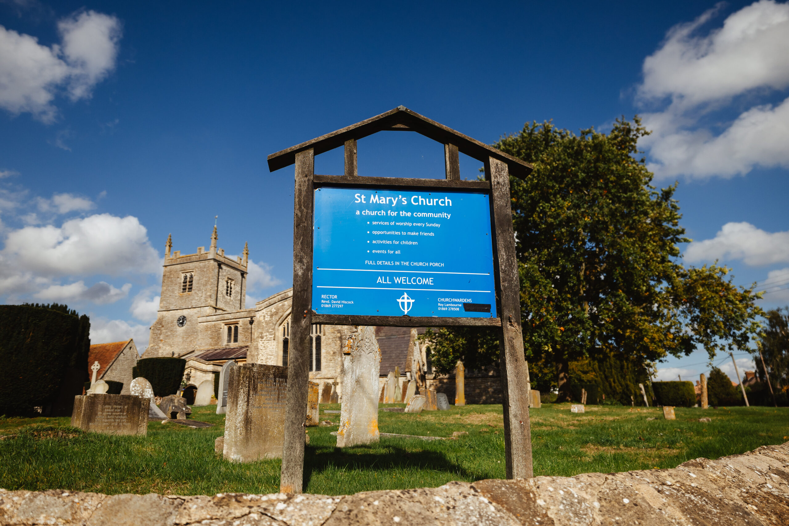 A sign in front of a church that says St Mary's Church. The sky behind is a lovely blue colour.