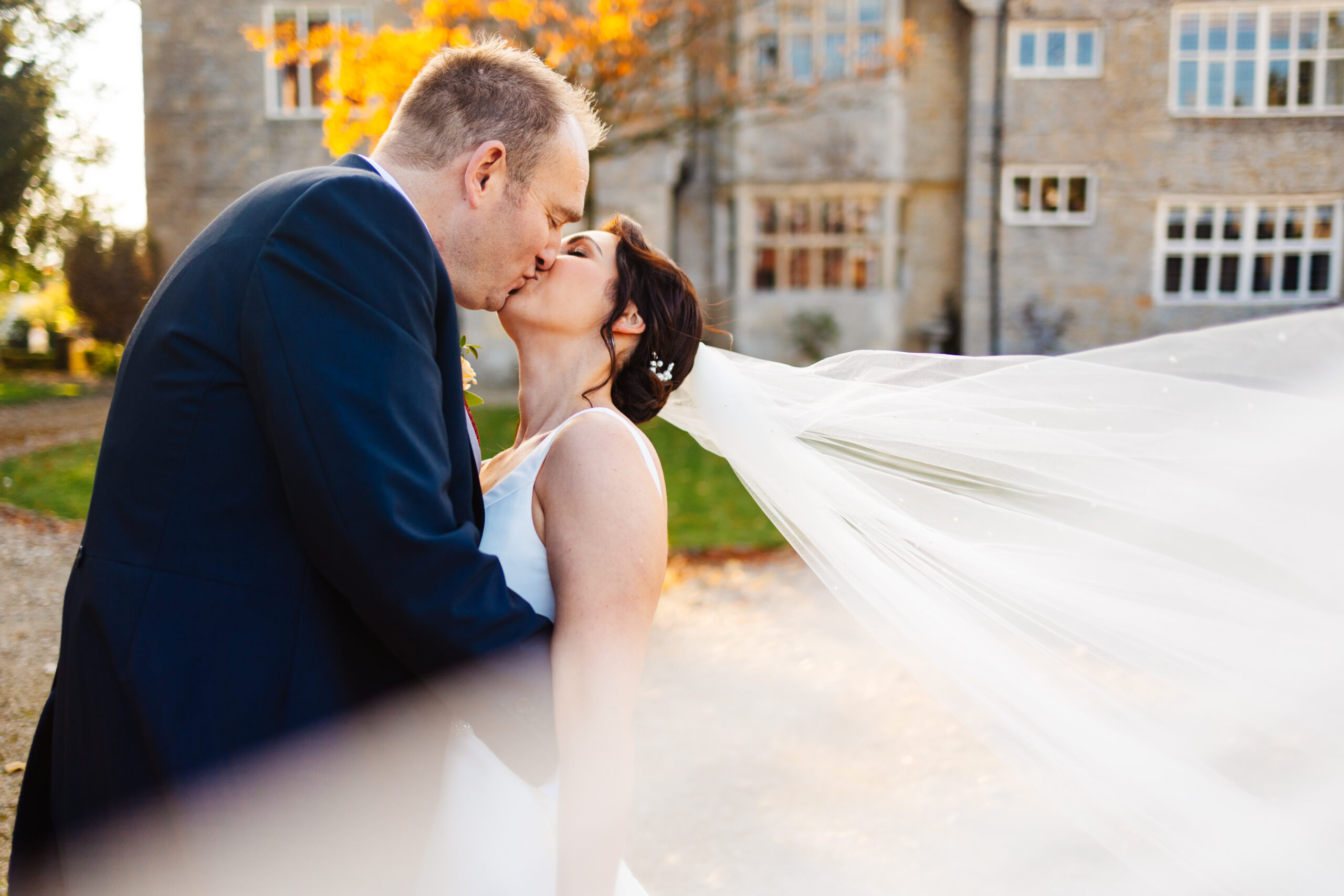 A photo of the bride and groom kissing. The bride's veil is floating in the wind.