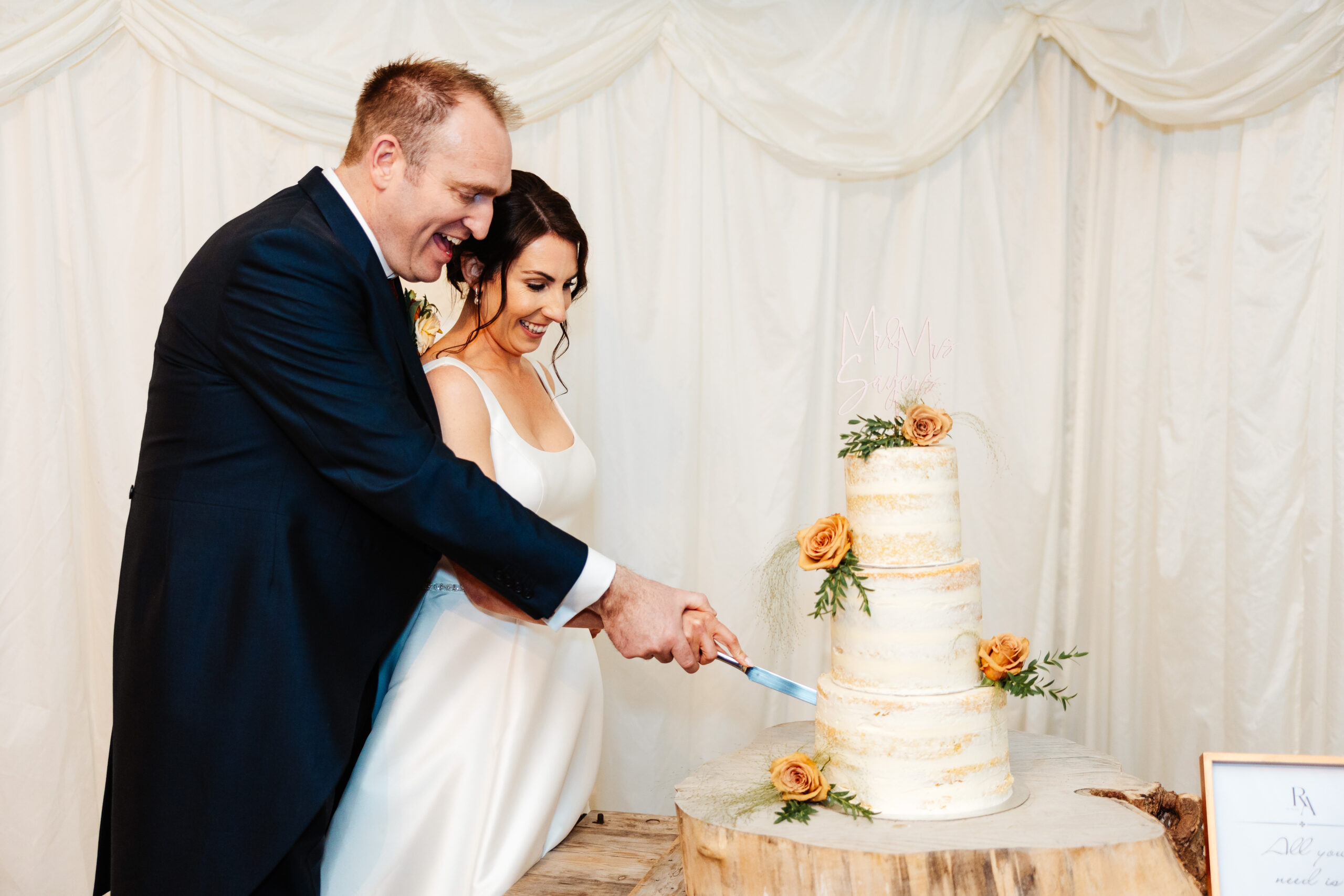 The bride and groom cutting the cake. The cake is three tiered naked cake and has four orange roses dotted on each layer for decoration.