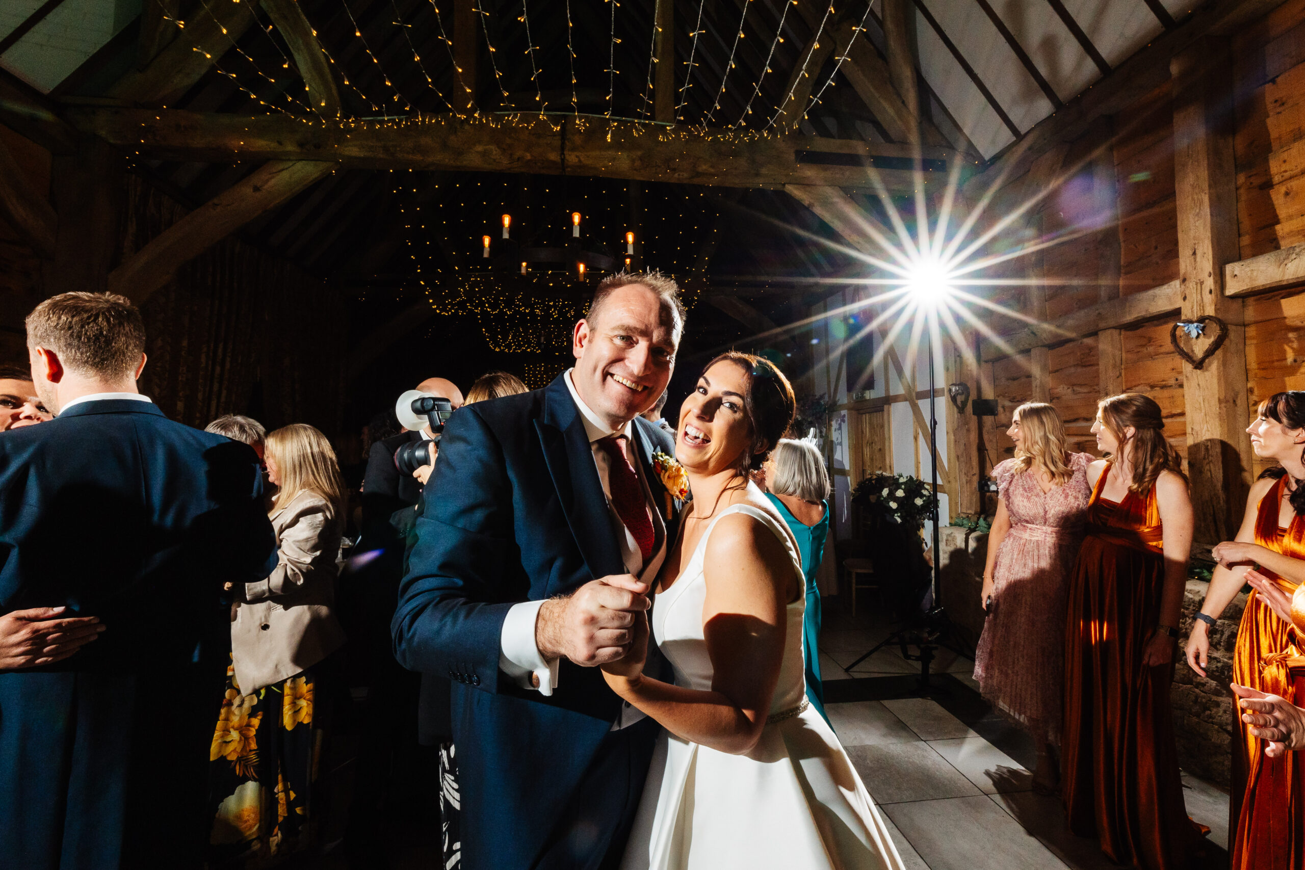 The newlyweds on the dancefloor. They are holding hands and dancing. You can see their friends in the background also dancing.