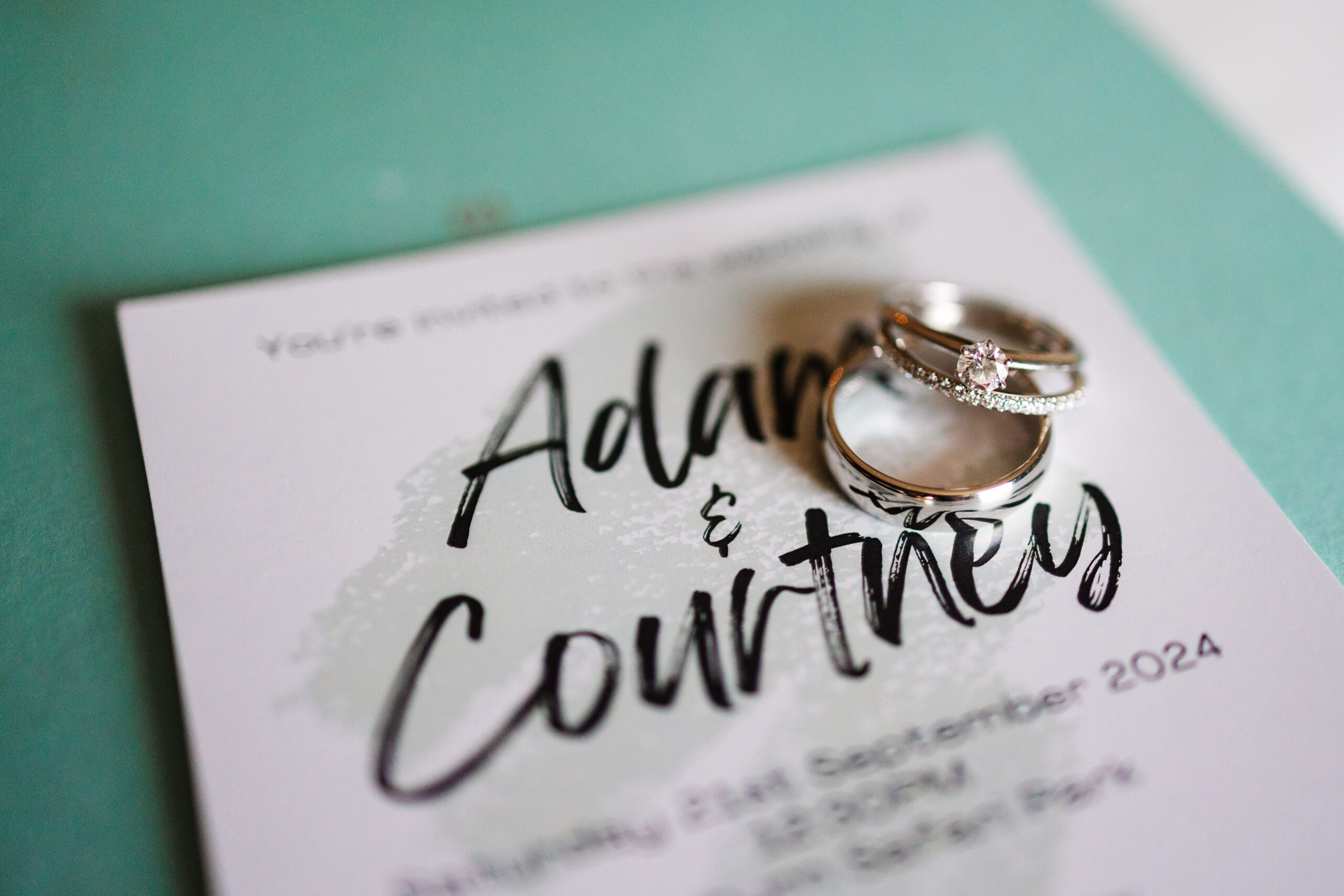 2 rings on top of the wedding invite of Adam and Courtney.