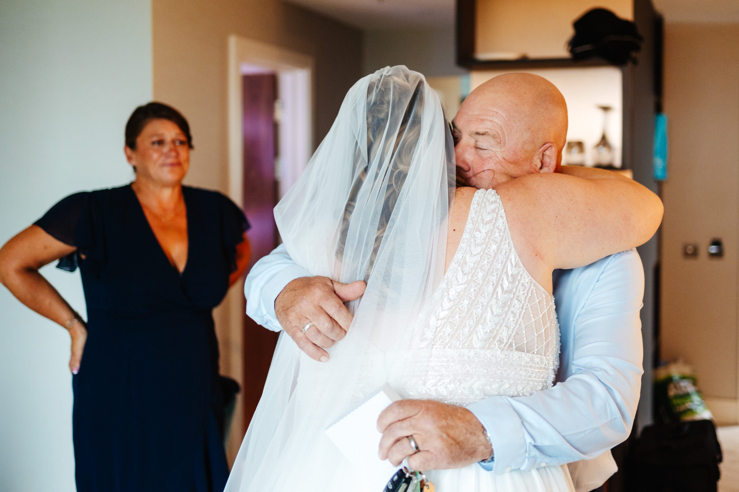 The father of the bride hugging the bride. He looks emotional and happy.