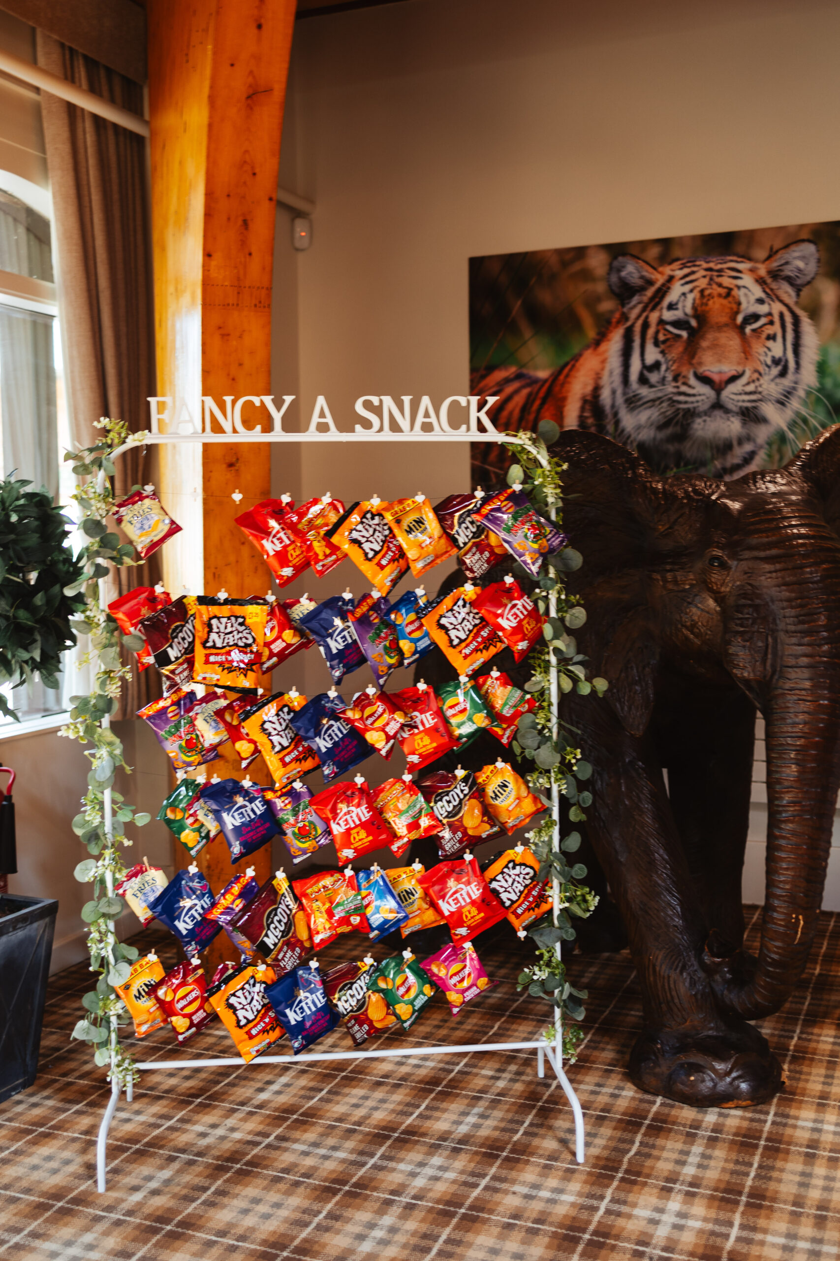 A large see through stand that has 'fancy a snack' written on the top. It is full of different flavoured crisps from Nik Naks to Kettle Chips and McCoys crisps.