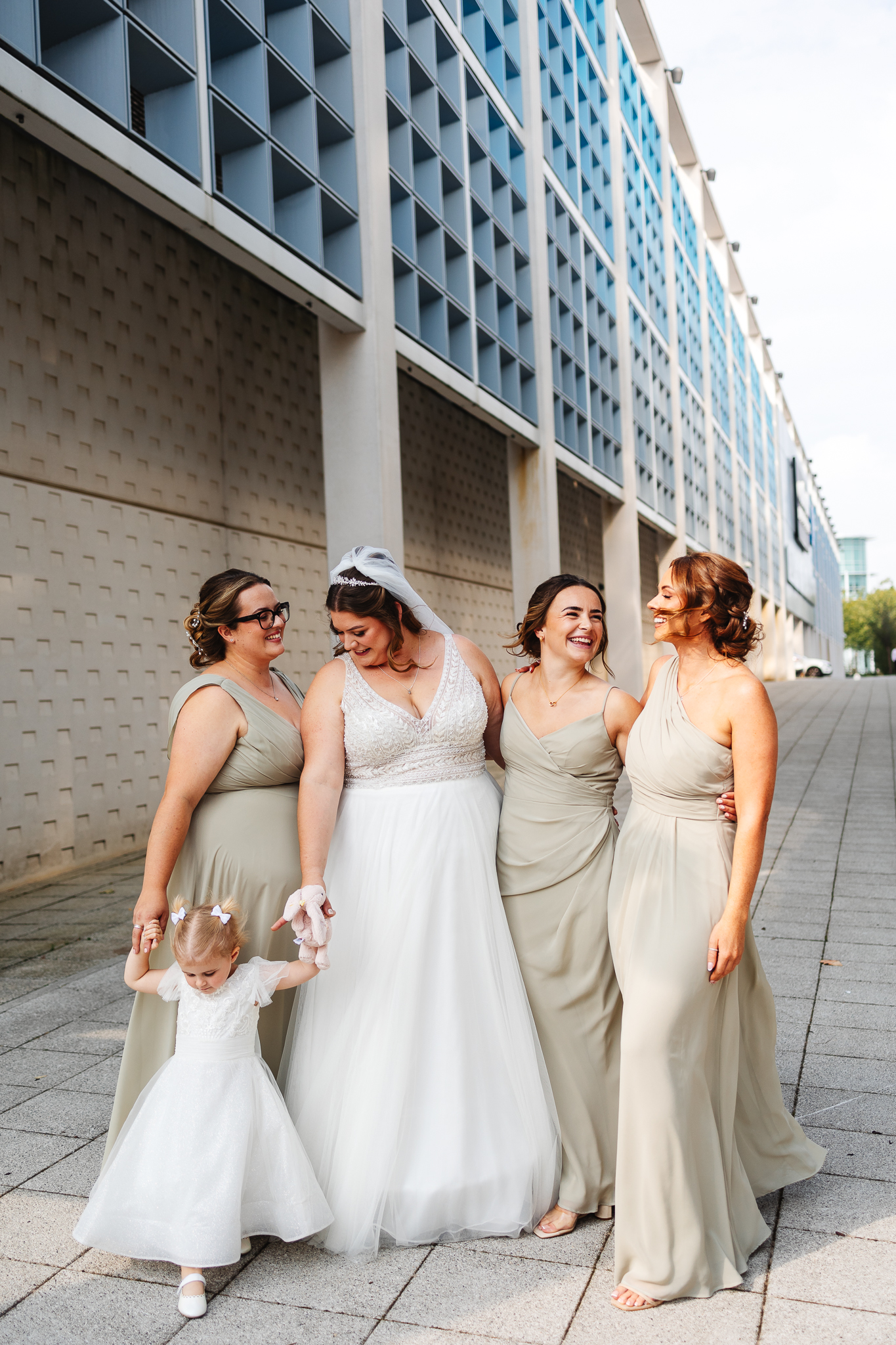 bridesmaids in jade dresses and bride stood together laughing outside the hotel la tour hotel in milton keynes