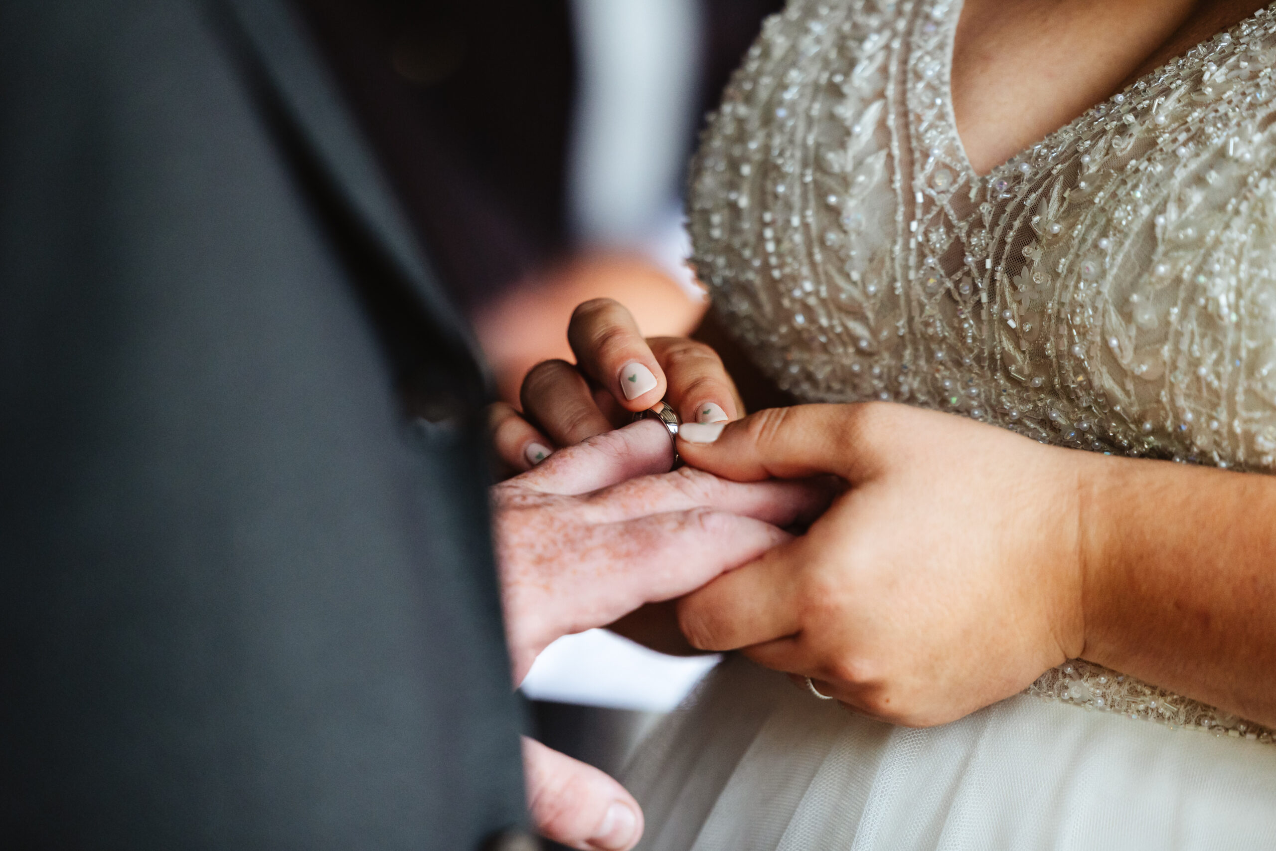 The bride putting a ring on her husband to be's finger. You can see the detailing of her sequinned and beaded dress.