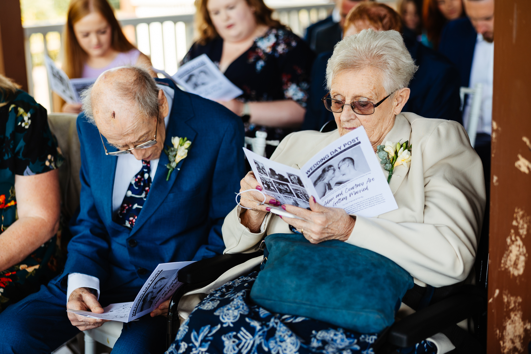 grandparents sat in chairs at a woburn safari park weddings, all in unison reading the wedding magazine print