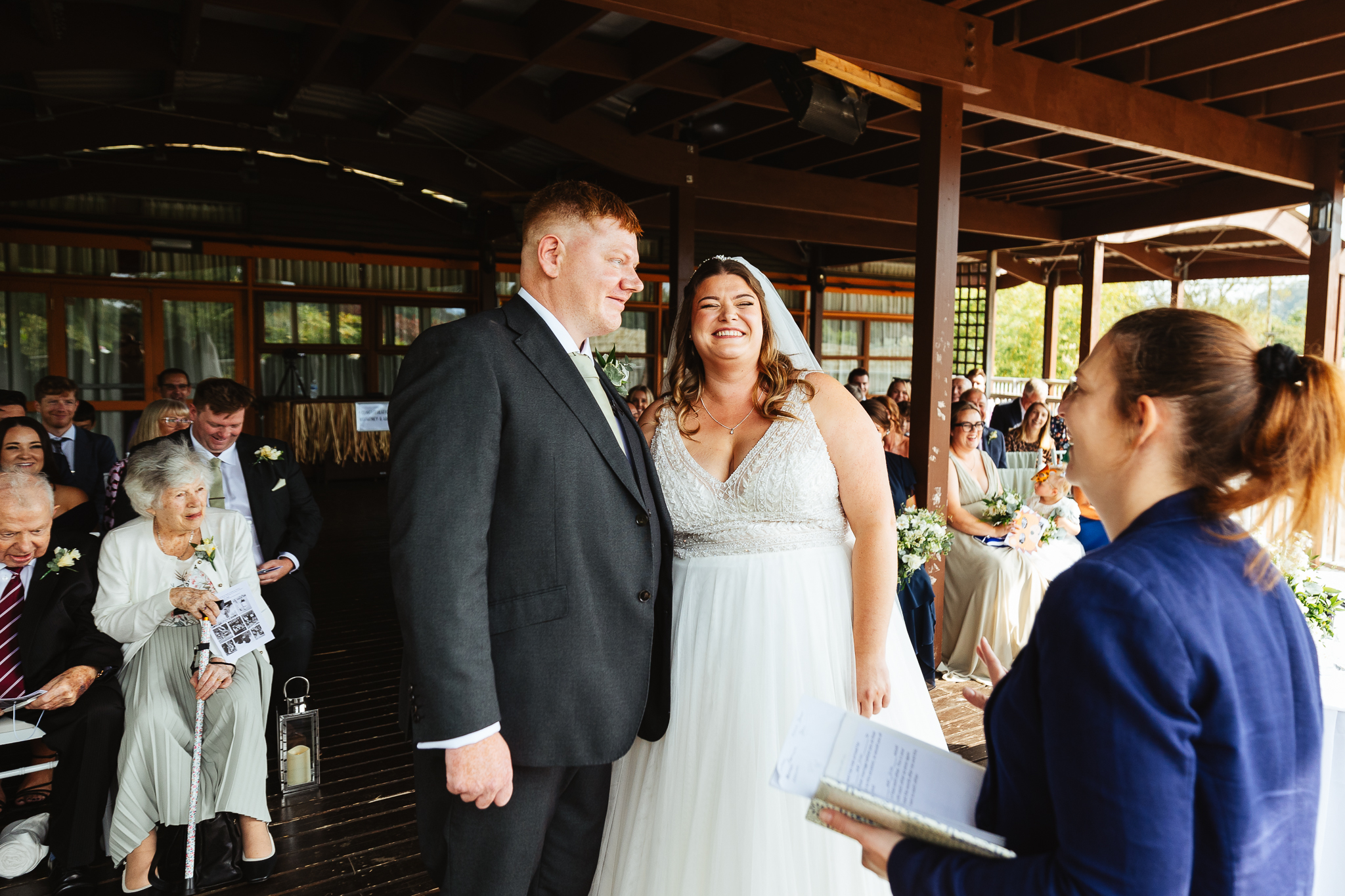 bride and groom at their woburn safari park wedding, standing together laughing in front of a wedding registrar, on the outside wooden platform overlooking animals.