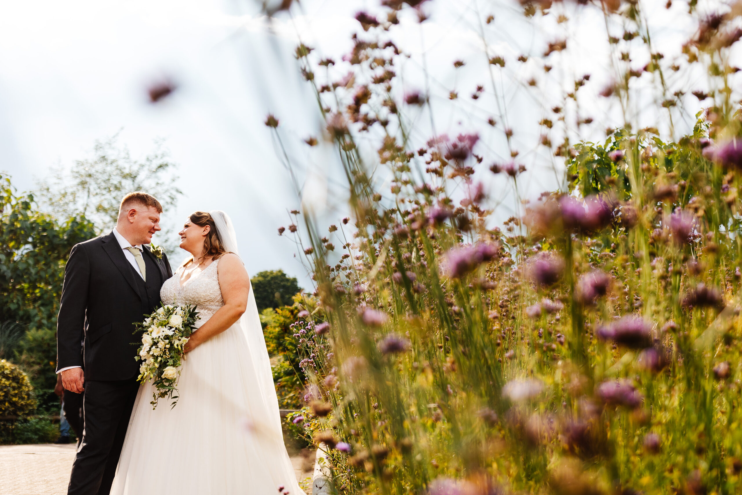 bride and groom stood amongst pink and purple flowers at woburn safari park 