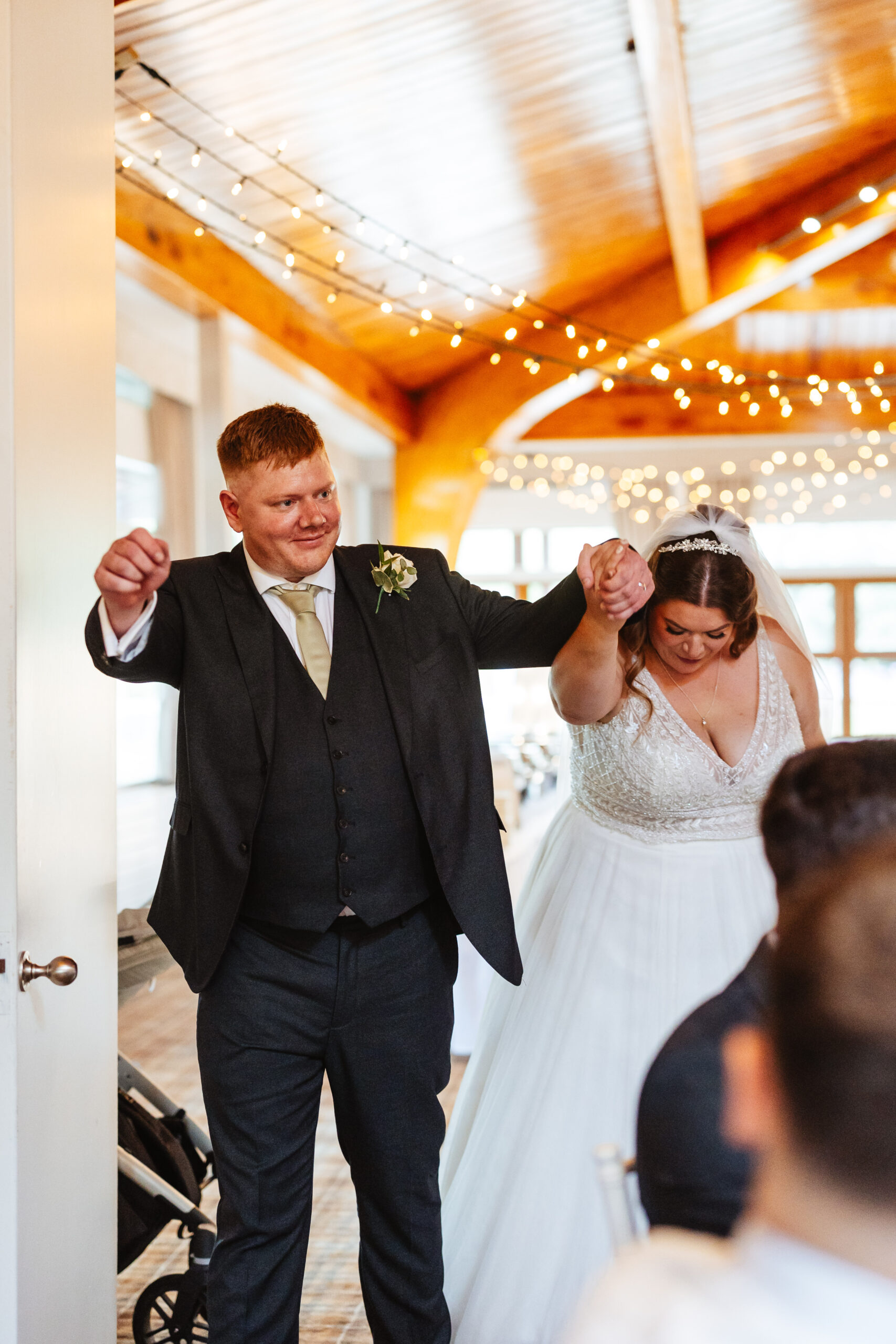 The bride and groom entering their wedding breakfast. They are holding hands and the groom has his other arm in the air. They are celebrating being the new Mr & Mrs Ball.